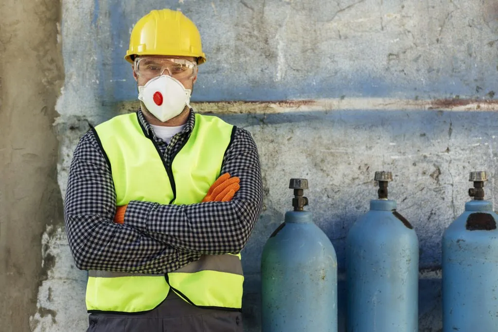 Gas engineer in hard hat and mask beside gas cylinders